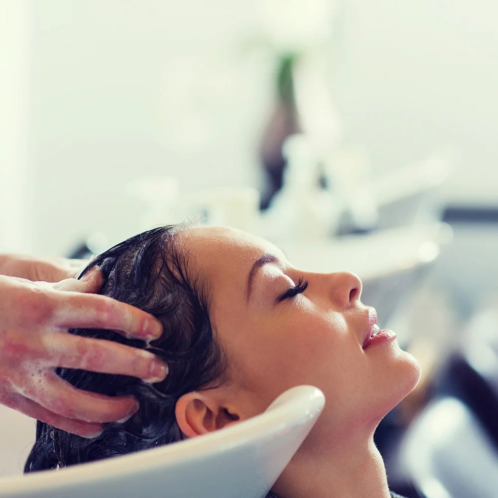 Persona lavando cabello en un lavacabezas, mostrando atención completa en el salón.
